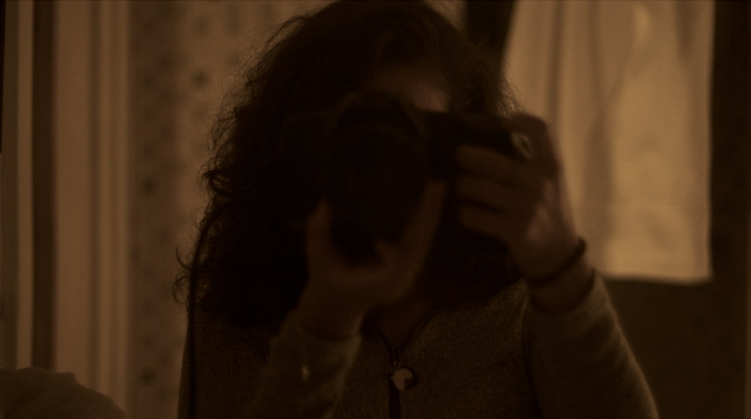 In&egrave;s photographing herself in a mirror, in low warm light